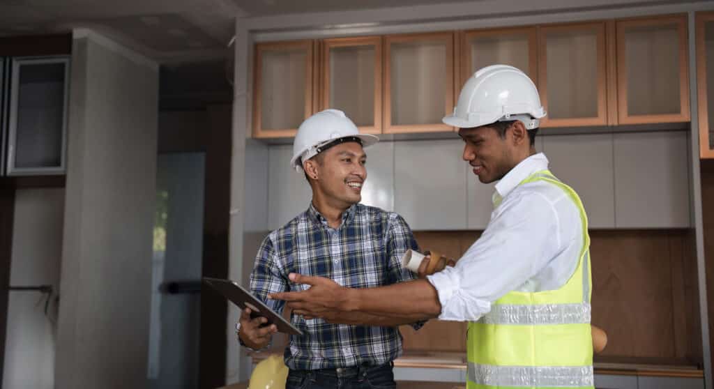 Consulting engineer and colleague discussing project details on a construction site, wearing safety gear and using a tablet.